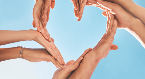 Mani di più persone che formano un cuore contro il cielo azzurro, simbolo di prevenzione e unione per la salute del cuore.