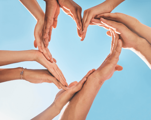 Mani di più persone che formano un cuore contro il cielo azzurro, simbolo di prevenzione e unione per la salute del cuore.