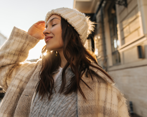 Donna sorridente con cappello di lana che si gode la luce del sole in una giornata invernale, simbolo dei benefici della vitamina D nei mesi bui.