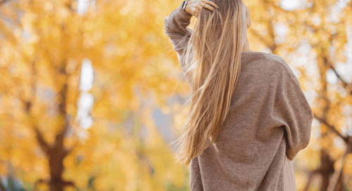 Donna di spalle con lunghi capelli biondi che brillano alla luce autunnale, simbolo di capelli sani, forti e luminosi durante la stagione autunnale.