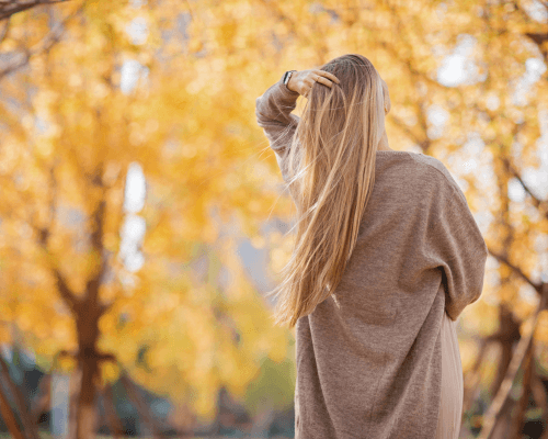 Donna di spalle con lunghi capelli biondi che brillano alla luce autunnale, simbolo di capelli sani, forti e luminosi durante la stagione autunnale.