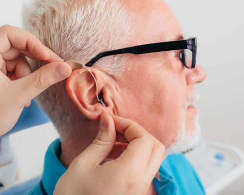 Operatore che aiuta un uomo anziano a indossare un apparecchio acustico durante una visita di controllo dell’udito.