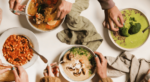Tavola vista dall’alto con diverse persone che condividono piatti colorati e salutari, simbolo di equilibrio e sostenibilità alimentare in occasione della Giornata Mondiale dell’Alimentazione.