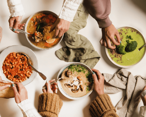 Tavola vista dall’alto con diverse persone che condividono piatti colorati e salutari, simbolo di equilibrio e sostenibilità alimentare in occasione della Giornata Mondiale dell’Alimentazione.
